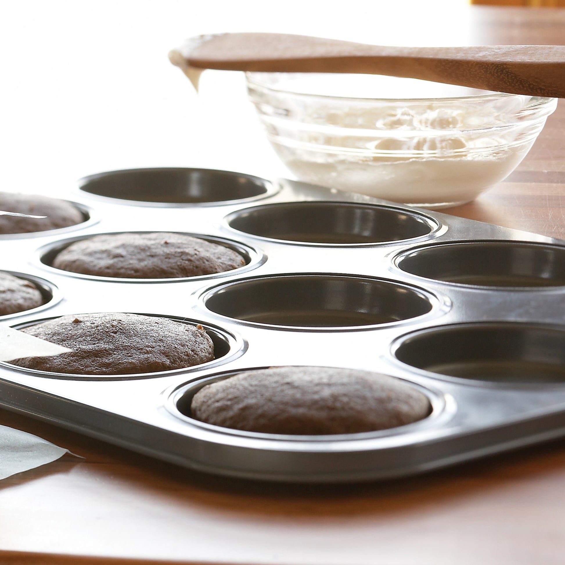 Dark gray non-stick pan with 12 shallow molds baking whoopie pies on wooden surface in kitchenware and bakeware collections