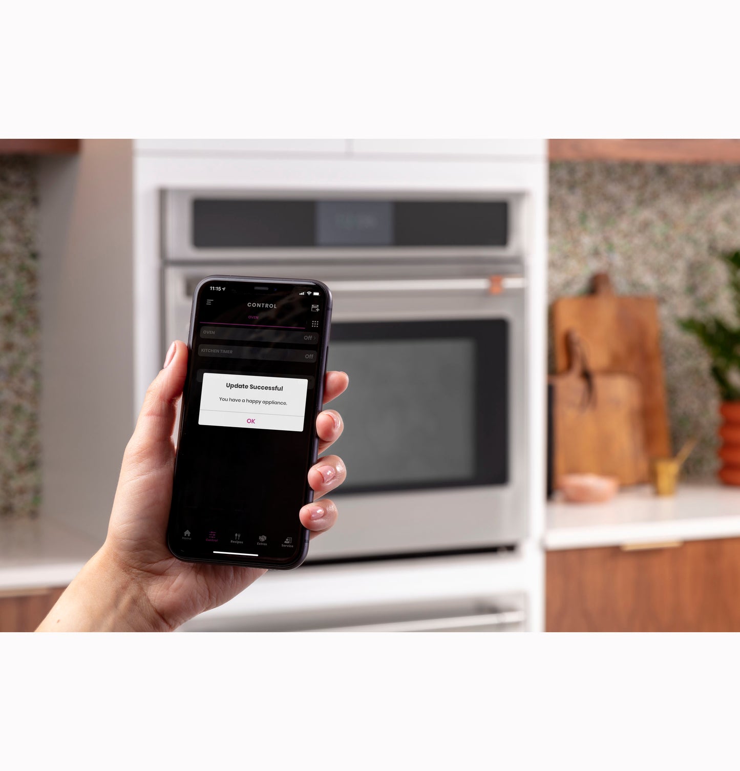Hand holding smartphone showing update success message in kitchen with built-in oven from appliances collection
