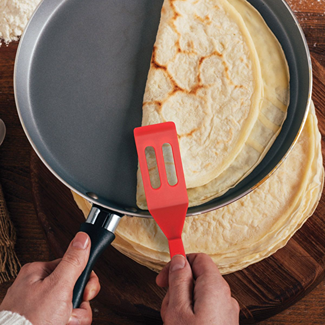 Hand using red silicone spatula to lift crepe off nonstick skillet in kitchenware and cooking utensils collections