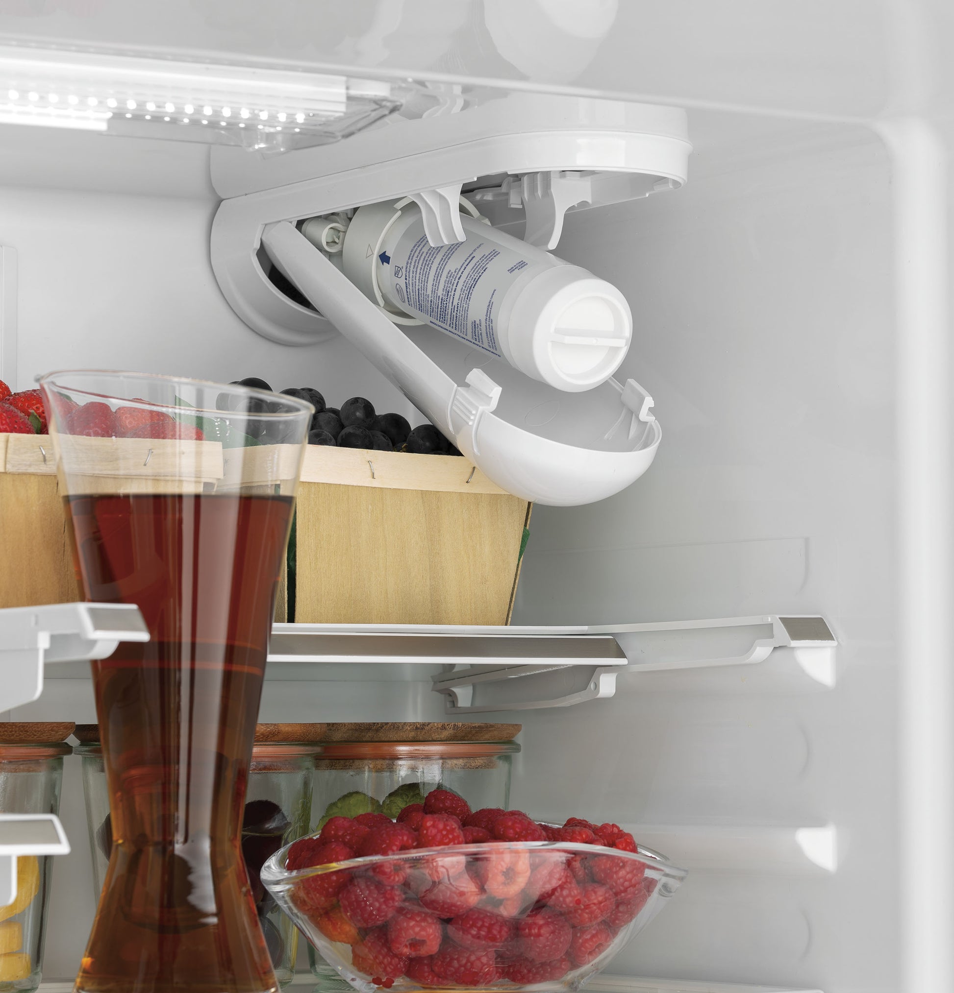 Interior shelf view of a refrigerator featuring an open water filter and fresh fruit in containers in kitchen appliances collection