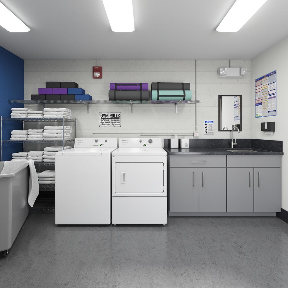 Commercial laundry area with white top-load washer, matching dryer, folded towels on rack, and gray cabinets with sink.