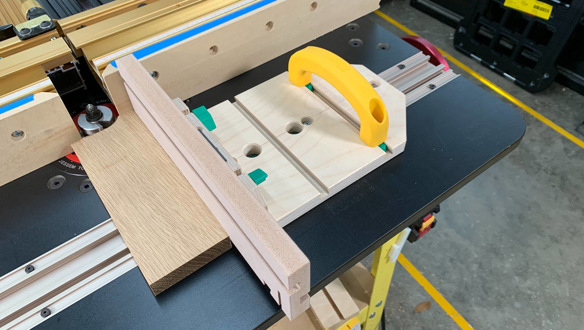 Yellow-handled push block with wooden base and jig on woodworking table for tools and home improvement use