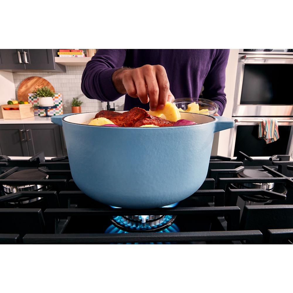 Blue cast iron pot cooking meat and potatoes on a gas burner in a modern kitchen setting with home improvement tools