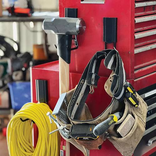 Black closed magnetic hooks holding a sledgehammer, tool belt, and yellow extension cord on red tool chest for home use