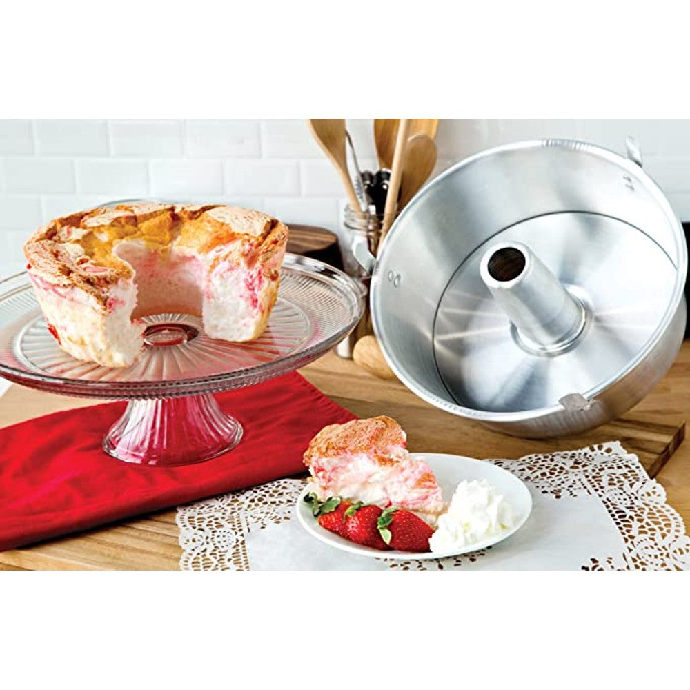Round aluminum loose bottom cake pan with center tube next to a partially sliced angel food cake on wood surface