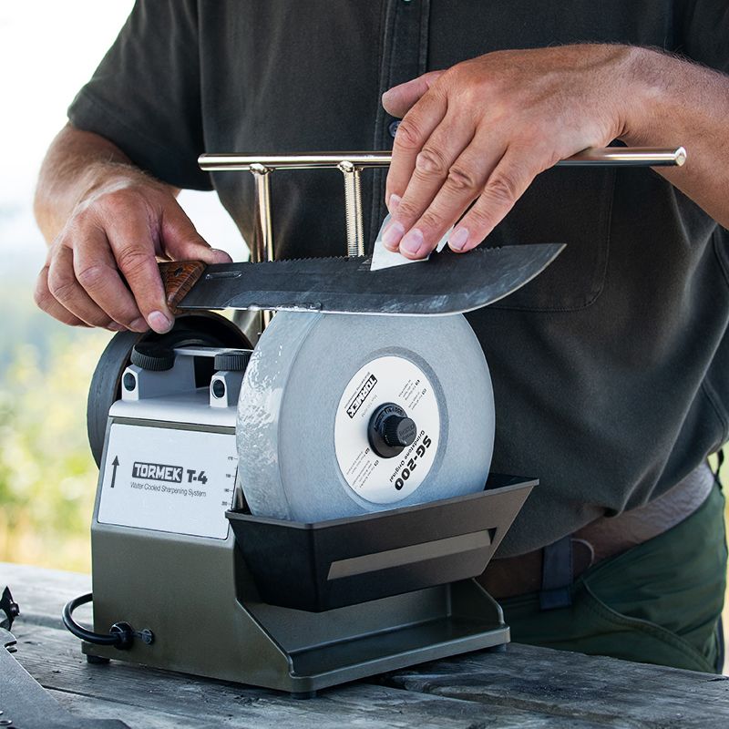 Person sharpening a large knife blade using a Tormek grinding machine with an extended support and micro adjustment feature
