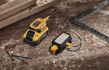 Yellow and black rechargeable LED task light connected to battery pack on wood workshop floor with tools nearby