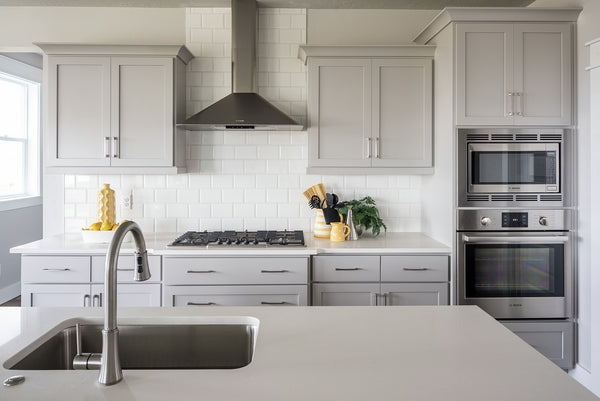 Contemporary kitchen with gray cabinetry, stainless steel wall oven and microwave, gas cooktop, and white subway tile backsplash