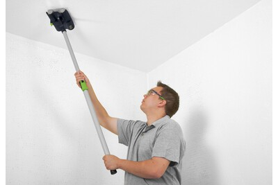 Person using a drywall sanding and wallpaper perforating tool with an extended handle for home improvement tasks.