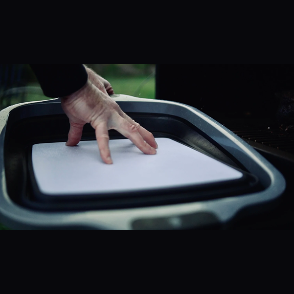 Hand placing white cutting board into black collapsible BBQ prep tub, a grilling accessory for outdoor living tasks