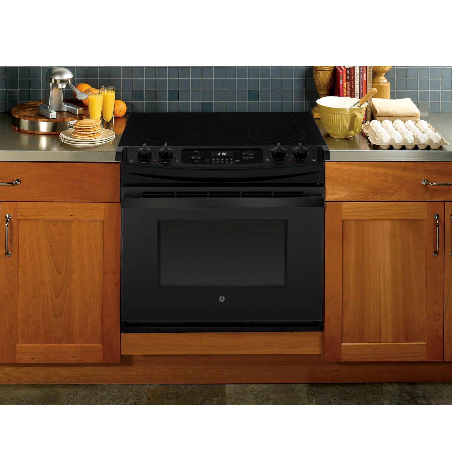 Black drop-in electric range with smooth cooktop and control knobs, installed between wooden kitchen cabinets in appliances collection