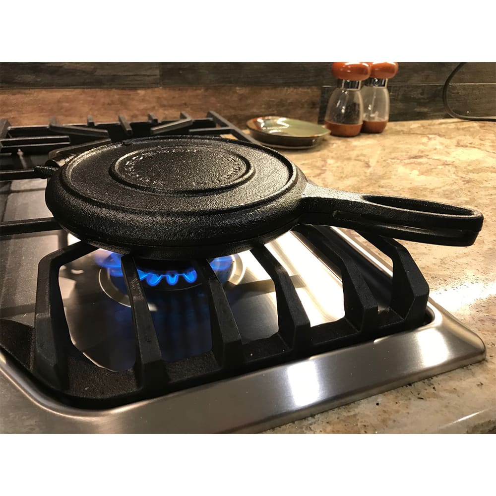 Cast iron stovetop waffle maker with long handle cooking on gas stove in modern kitchen setting