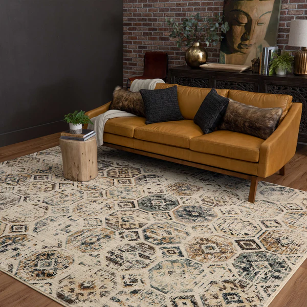 Beige textured rug with hexagonal and distressed geometric patterns in muted blue, tan, and gray tones beneath a modern leather sofa.