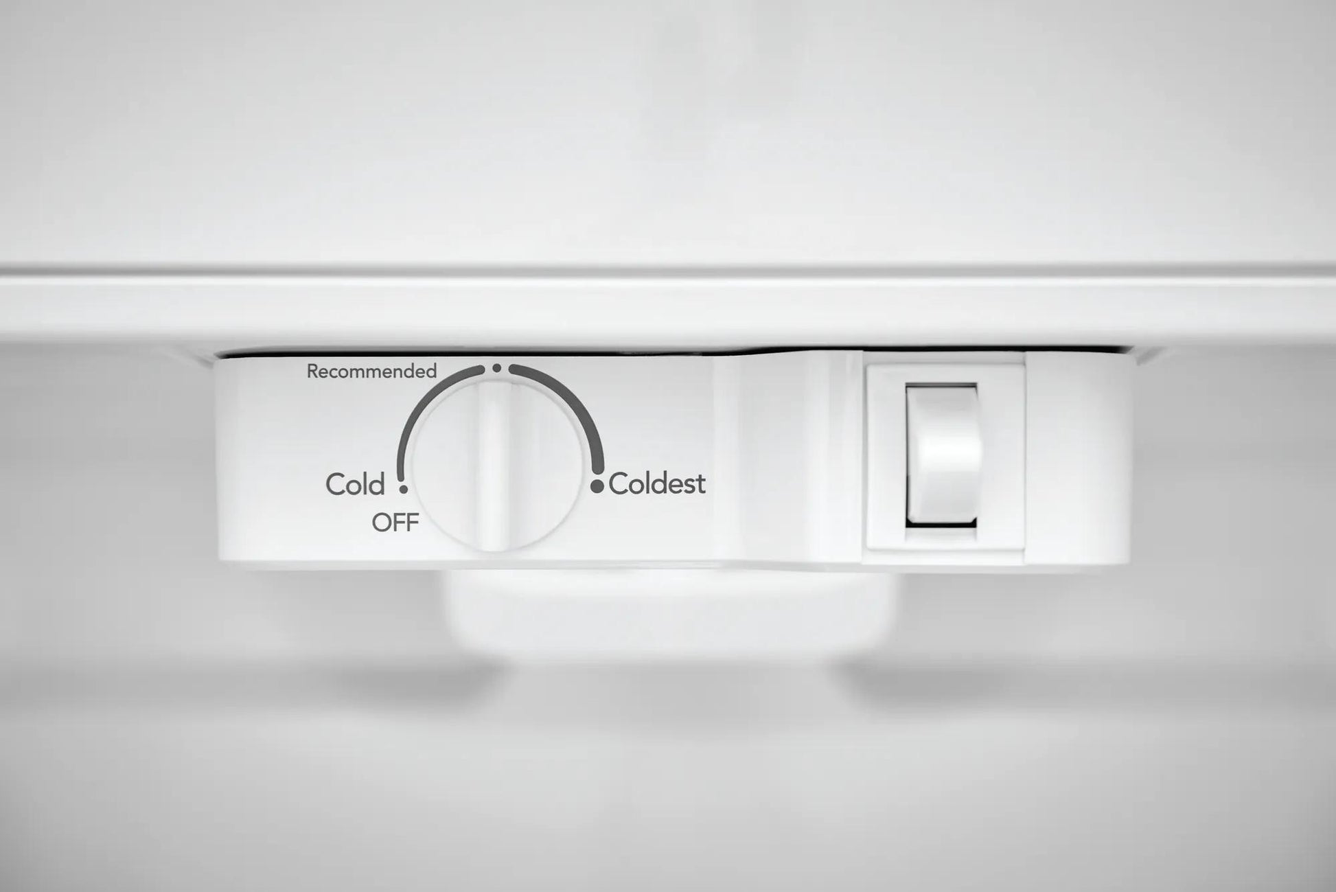 Close-up of white temperature control dial and light switch inside a top freezer refrigerator in appliances collection