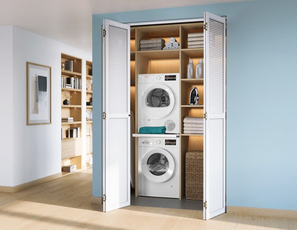 Stacked white compact Bosch washer and dryer set in built-in wooden closet with shelves and folded towels