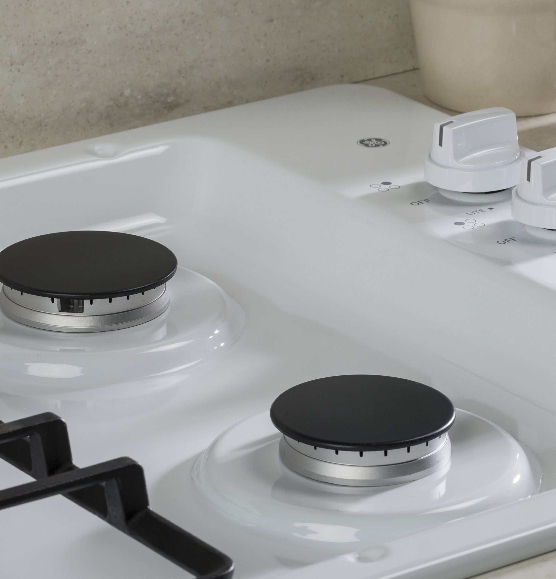Close-up of white built-in gas cooktop with black burner caps and white control knobs in kitchen setting