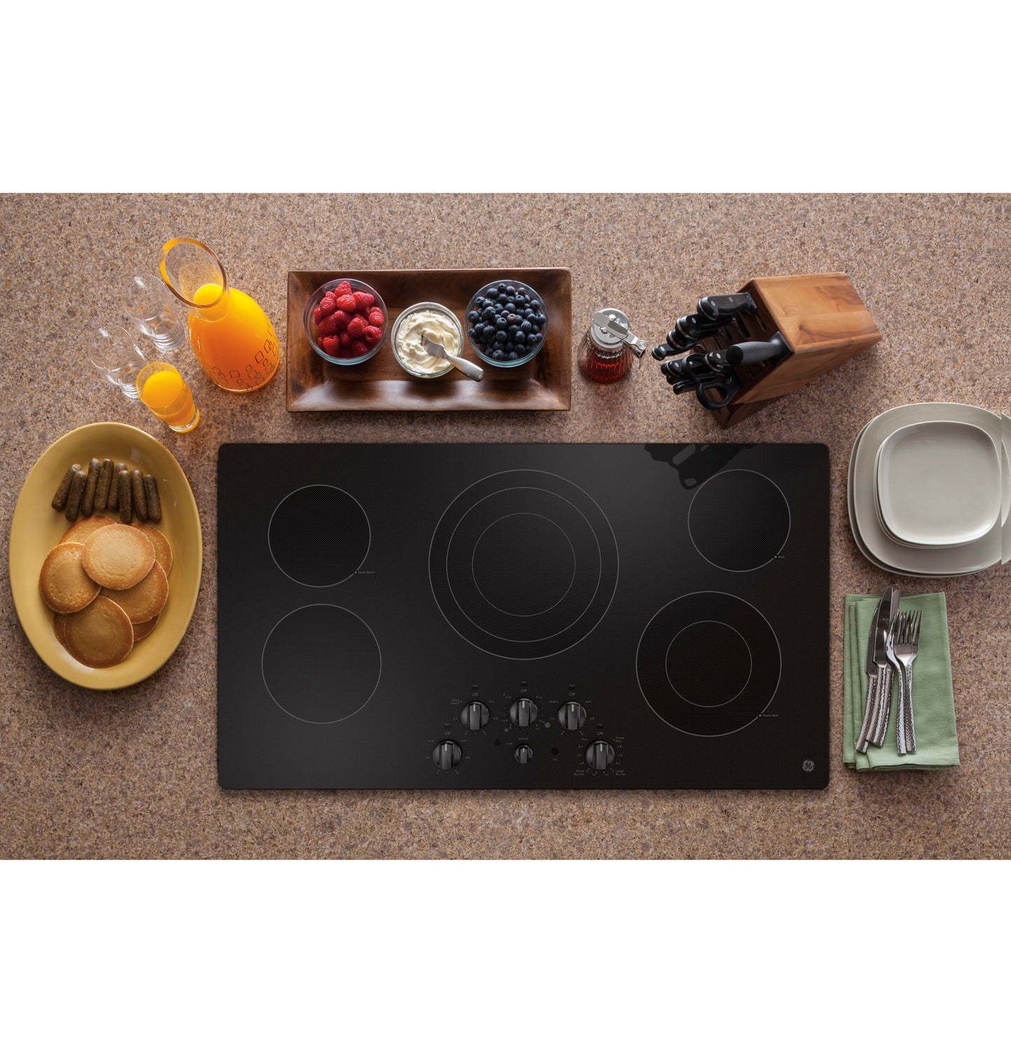 Black built-in electric cooktop with knob controls surrounded by breakfast items and kitchenware on countertop