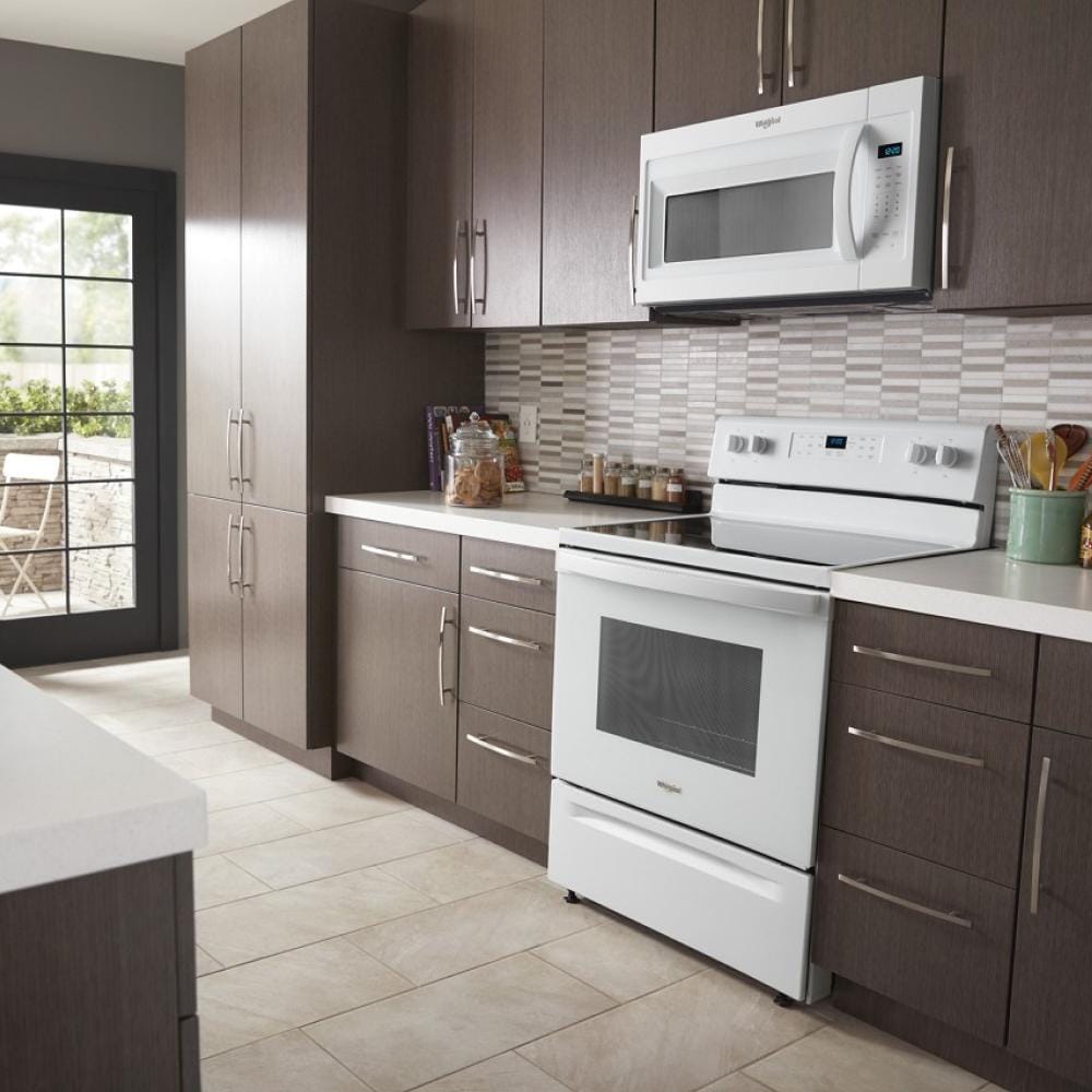 Modern kitchen with white microwave hood mounted above electric stove and dark wood cabinetry in appliance setting