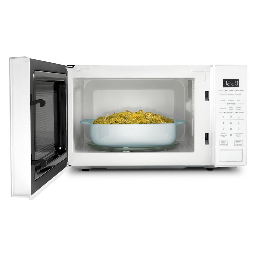White countertop microwave with open door showing pasta in a white ceramic dish and digital control panel
