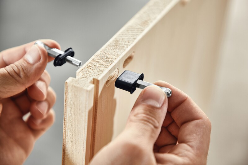Hands installing black and metal center panel connectors on light wood panels for woodworking tool accessories and home improvement projects