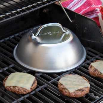 Aluminum cheese melting dome with handle on grill surrounded by burger patties in kitchen gadgets collection