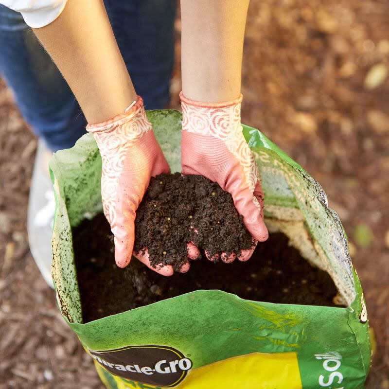 Hands wearing pink gardening gloves holding rich soil over an open bag of all-purpose garden soil for outdoor living projects