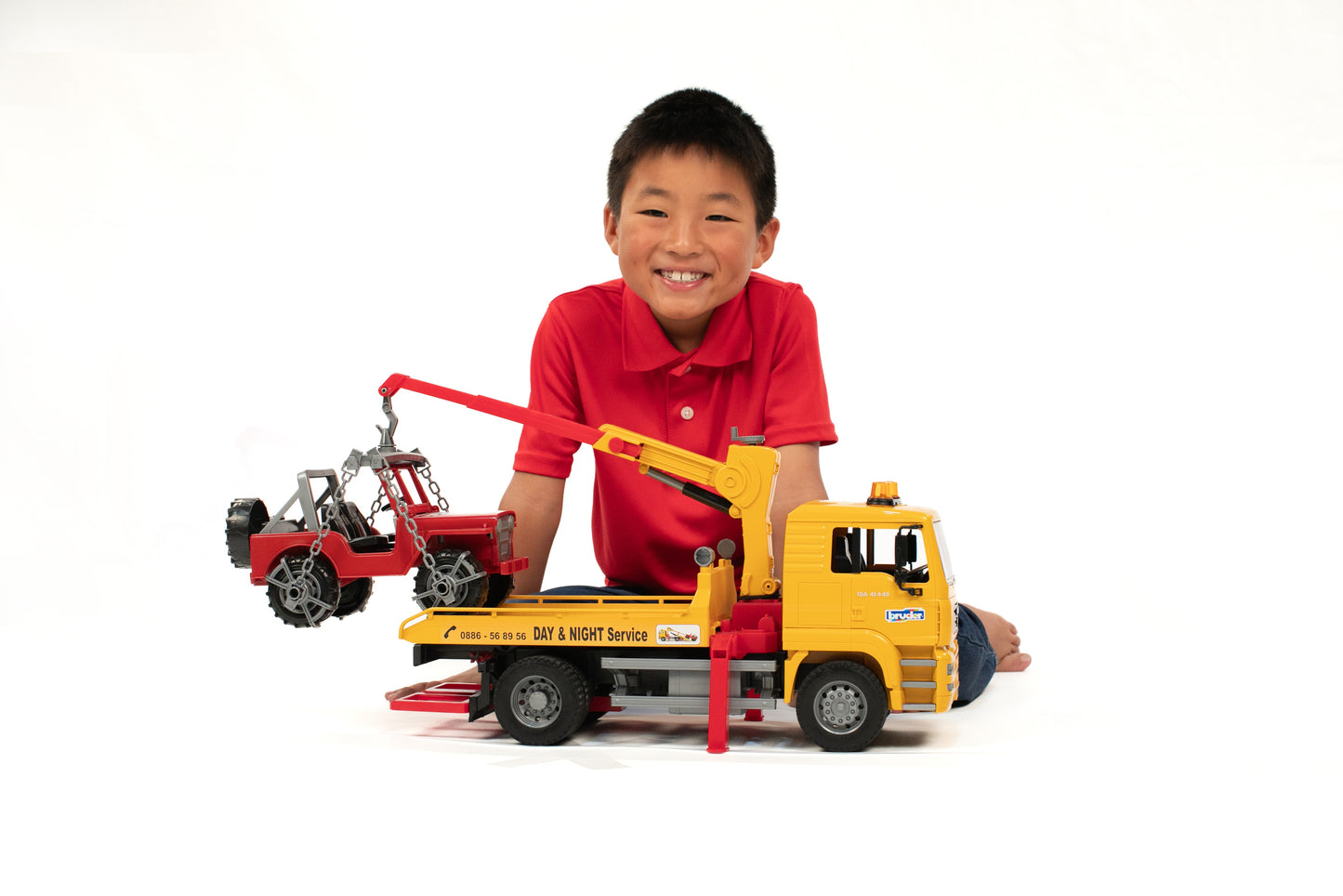 Young boy playing with yellow Bruder MAN TGA tow truck lifting red cross country vehicle toy