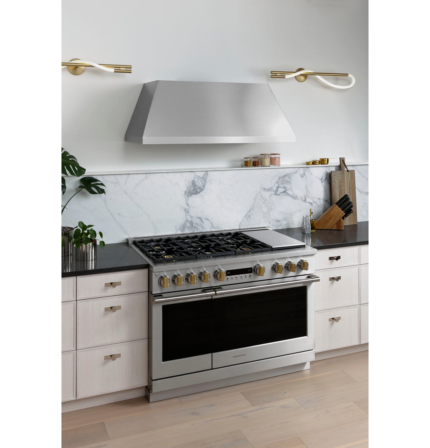 Modern stainless steel professional hood installed above gas range in kitchen with light cabinetry and marble backsplash