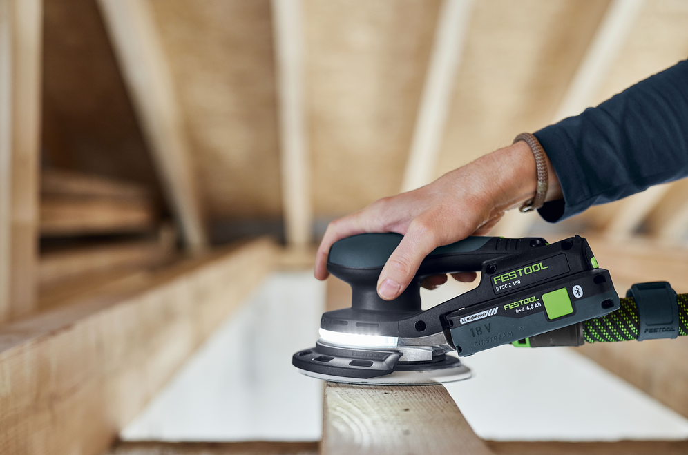 Cordless orbital sander with LED light sanding wooden beam in unfinished interior, part of woodworking and power tools collection