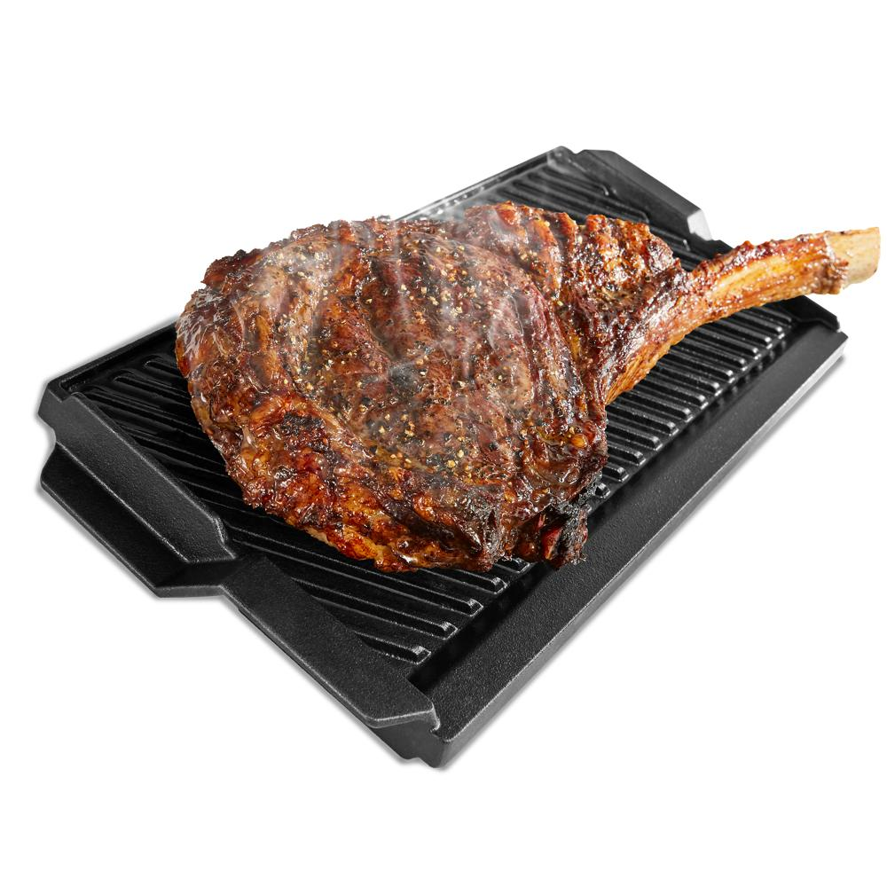 Grilled seasoned bone-in steak resting on a black cast iron grill pan from kitchenware and ranges collections