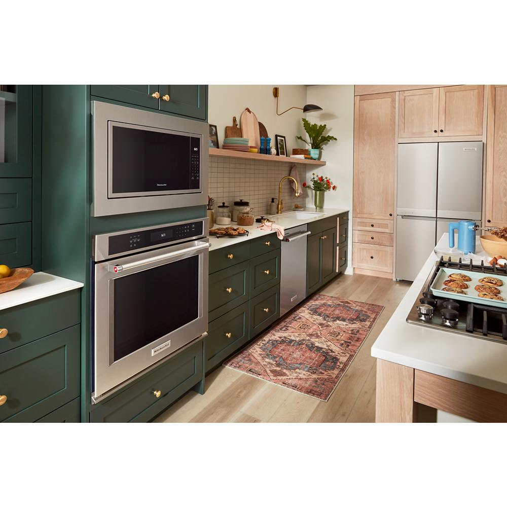 Built-in stainless steel microwave above double wall oven integrated into green cabinetry in modern kitchen setting