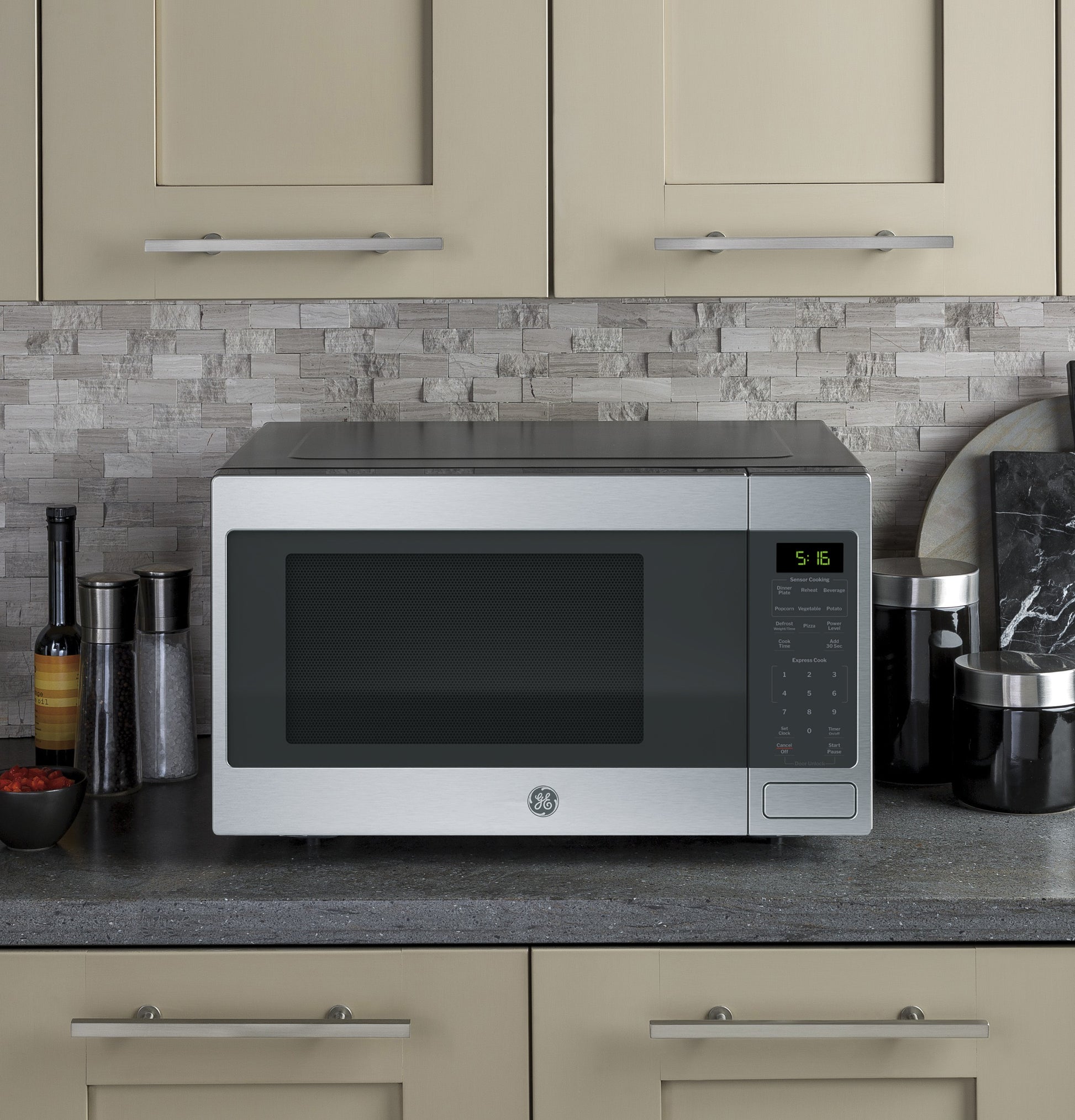 Stainless steel countertop microwave with digital display and control panel in modern kitchen setting with stone backsplash