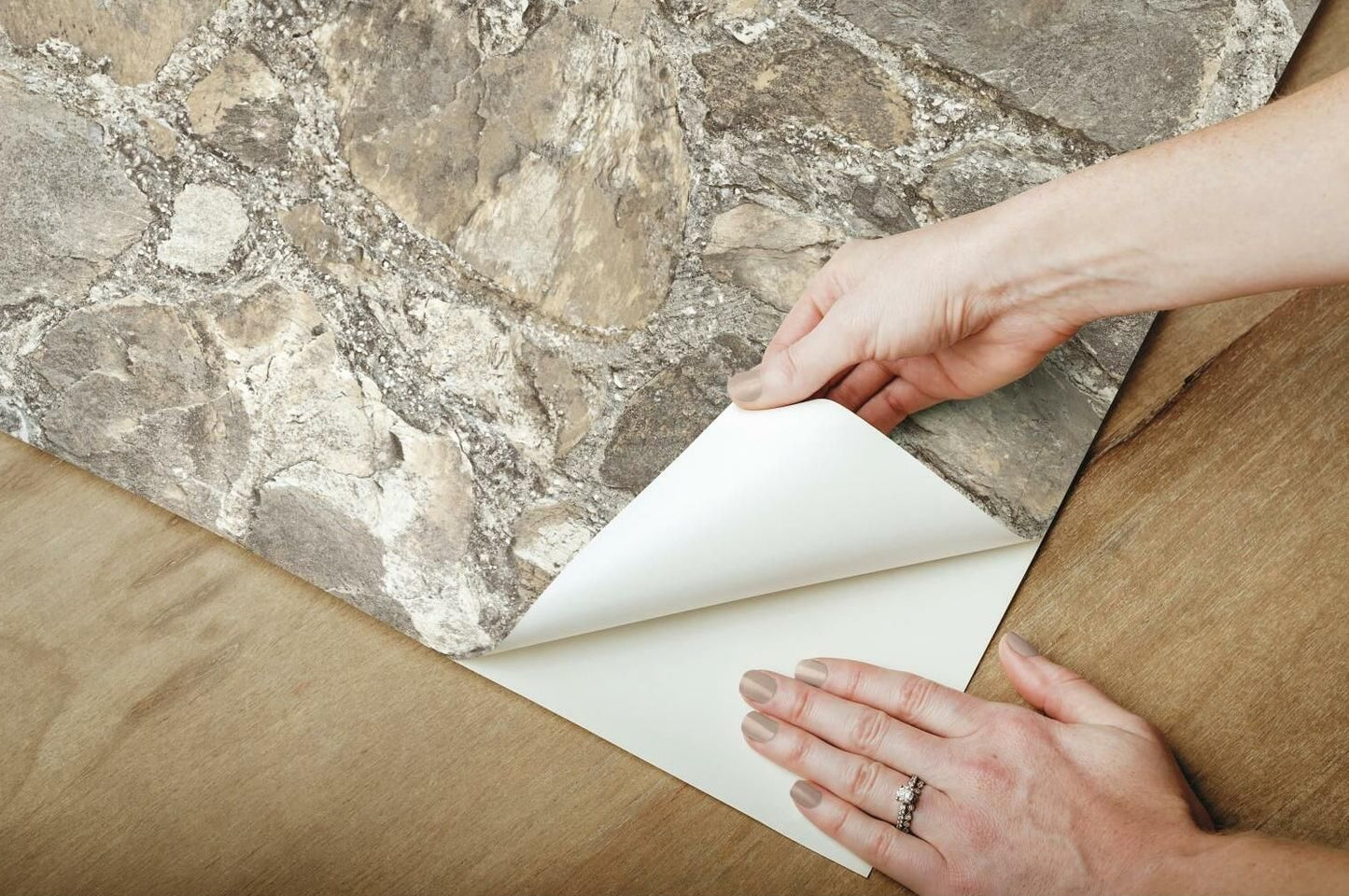 Hands applying weathered stone peel and stick wallpaper on wooden surface for home improvement project