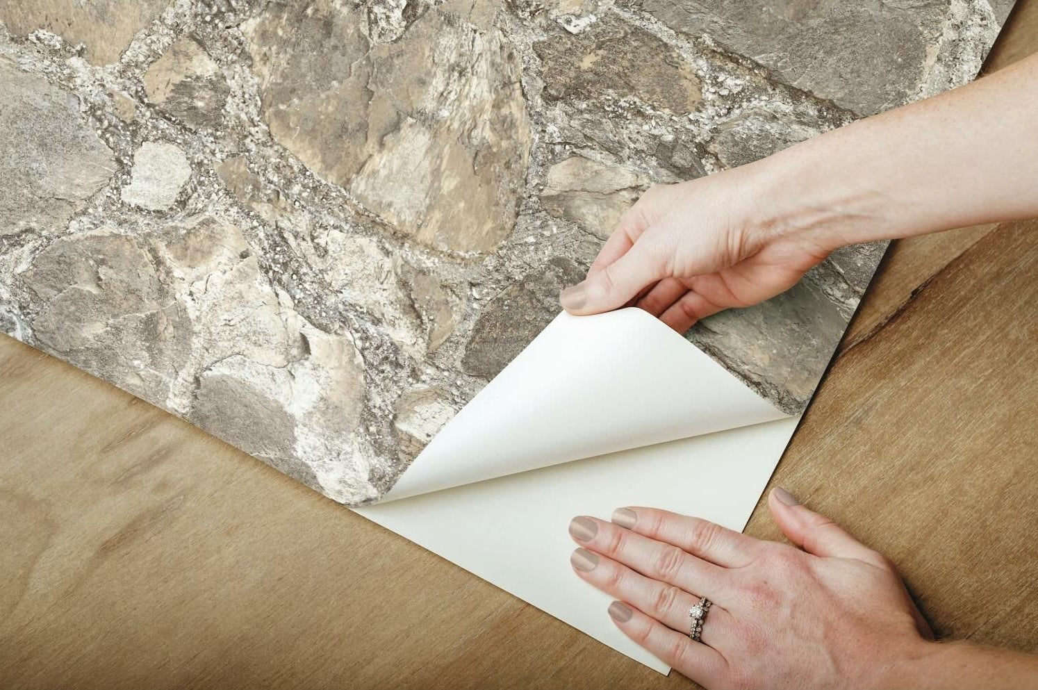 Hands applying weathered stone peel and stick wallpaper on wooden surface for home improvement project