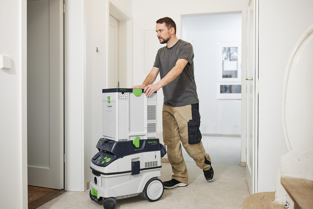 Man maneuvering a modular Festool filtration unit with green accents for dust control in a home improvement setting