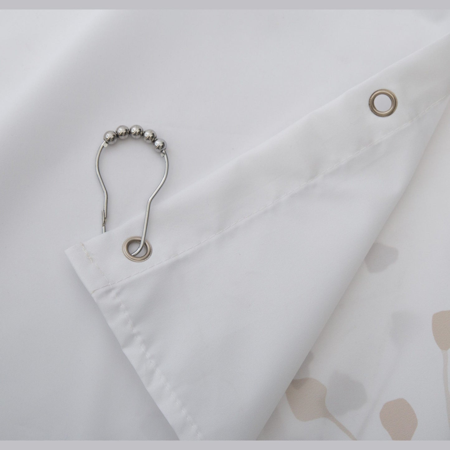 Close-up of white fabric shower curtain corner with metal grommets and silver ball-style hanging hook for bathroom use