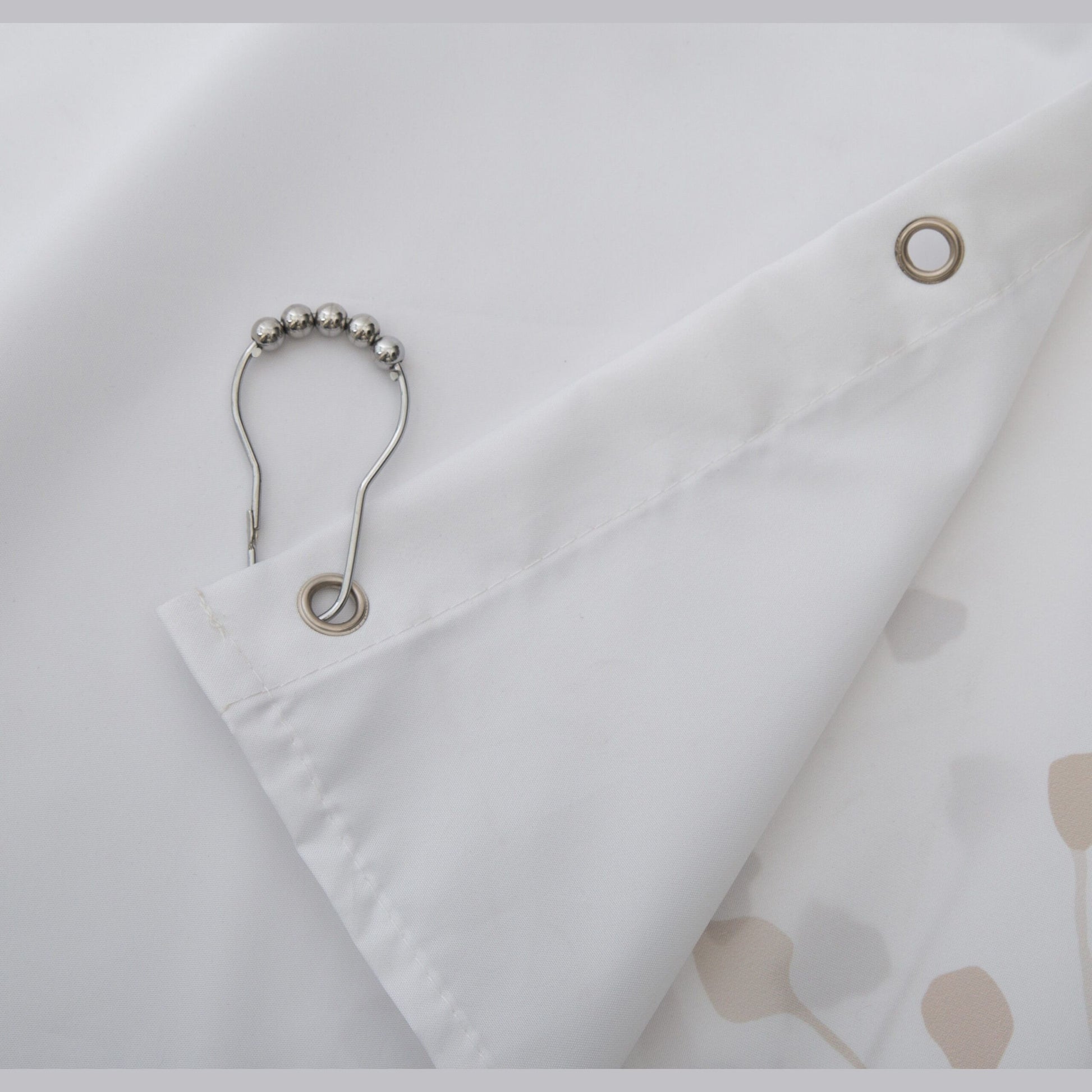 Close-up of white fabric shower curtain corner with metal grommets and silver ball-style hanging hook for bathroom use