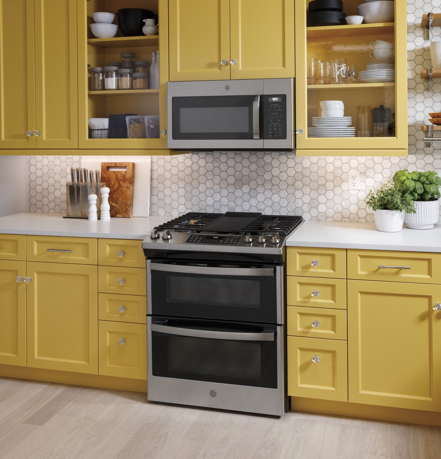 Fingerprint resistant over-the-range microwave above stainless steel double oven in yellow kitchen with hex tile backsplash