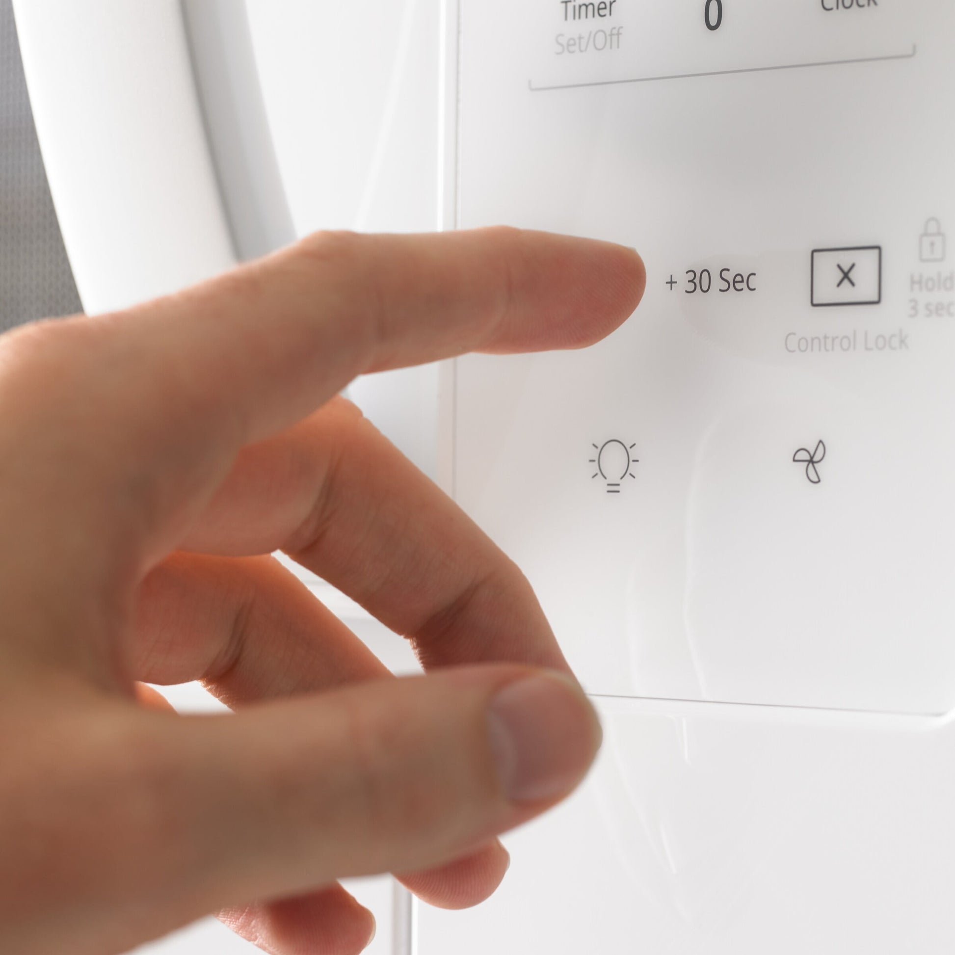Hand pressing electronic touch control panel on white microwave from over the range appliances collection