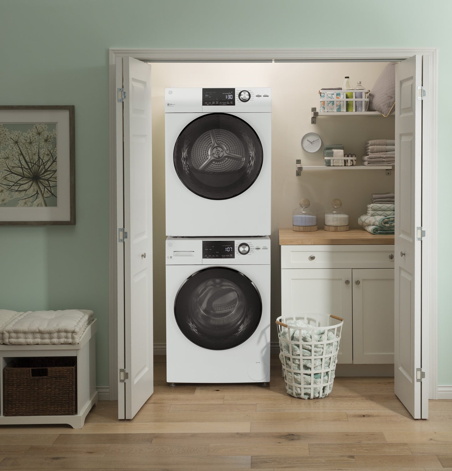Stacked white front-load washer and electric dryer in a compact laundry closet with shelves and a laundry basket nearby