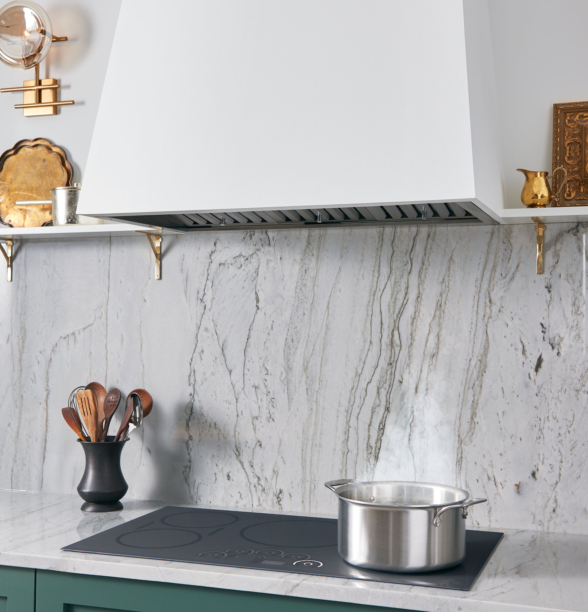 Modern kitchen setup with marble backsplash, green cabinetry, induction cooktop, steaming pot, and white range hood from Appliances collection