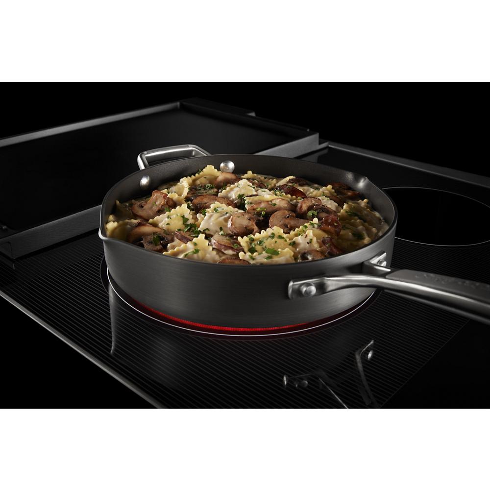 Black glass cooktop with glowing heating element and sauté pan cooking mushroom and herb pasta meal