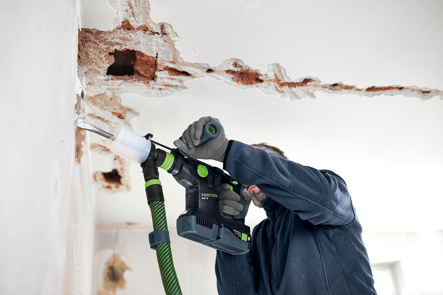 Person using Festool auxiliary handle on cordless rotary hammer drill during wall chiseling for home improvement tasks