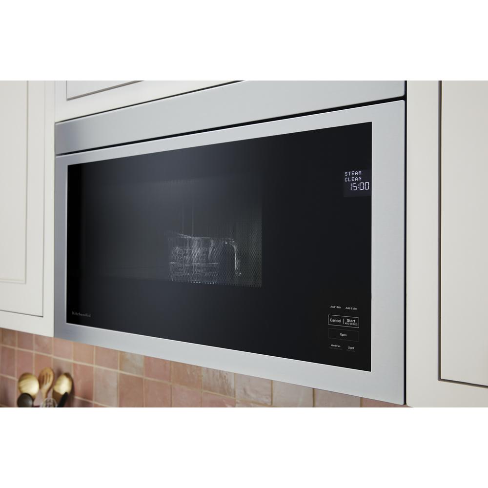 Stainless steel built-in microwave with digital touchscreen control panel mounted between kitchen cabinets