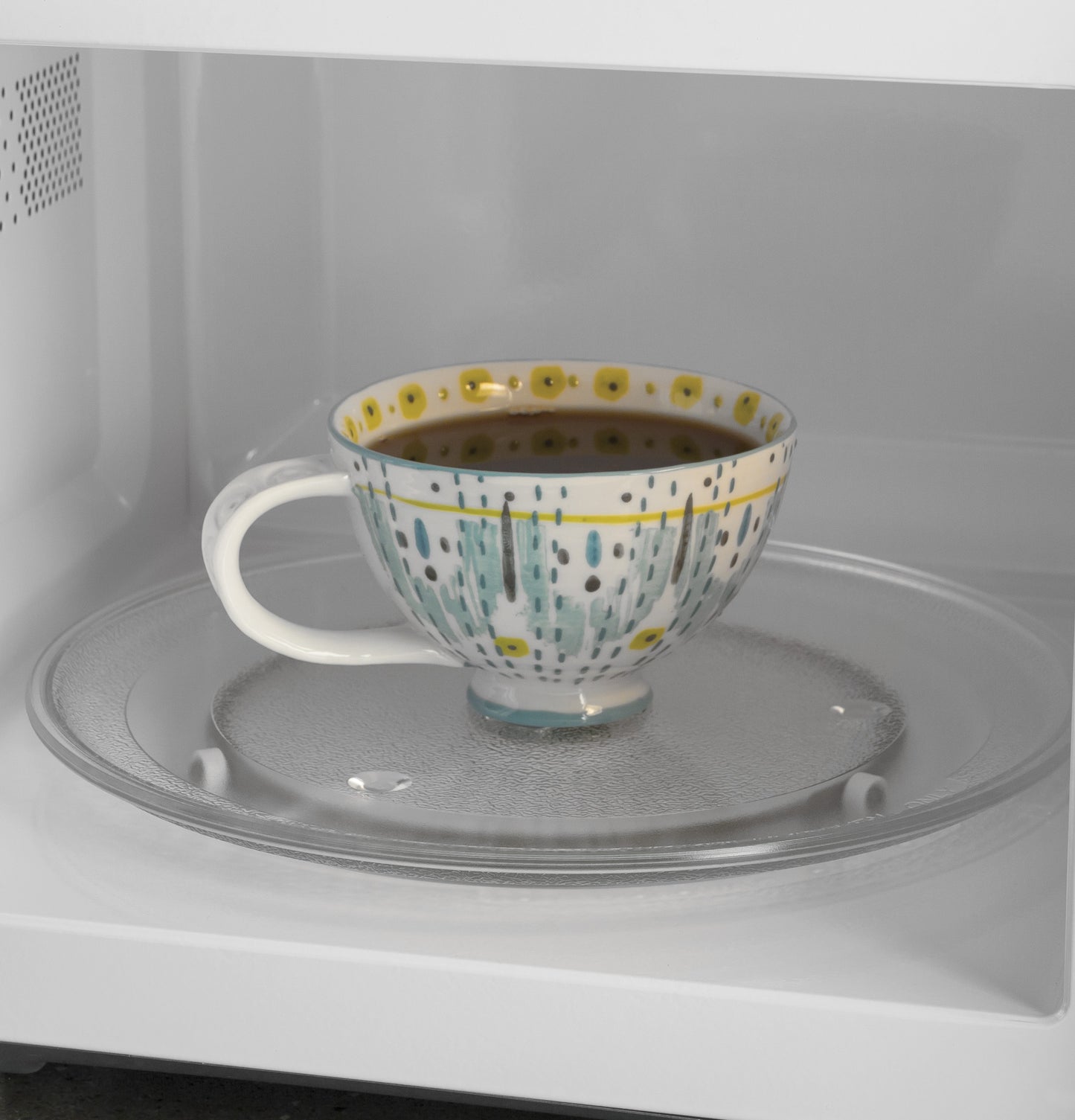 Interior of countertop microwave oven with patterned ceramic mug filled with dark liquid on glass turntable