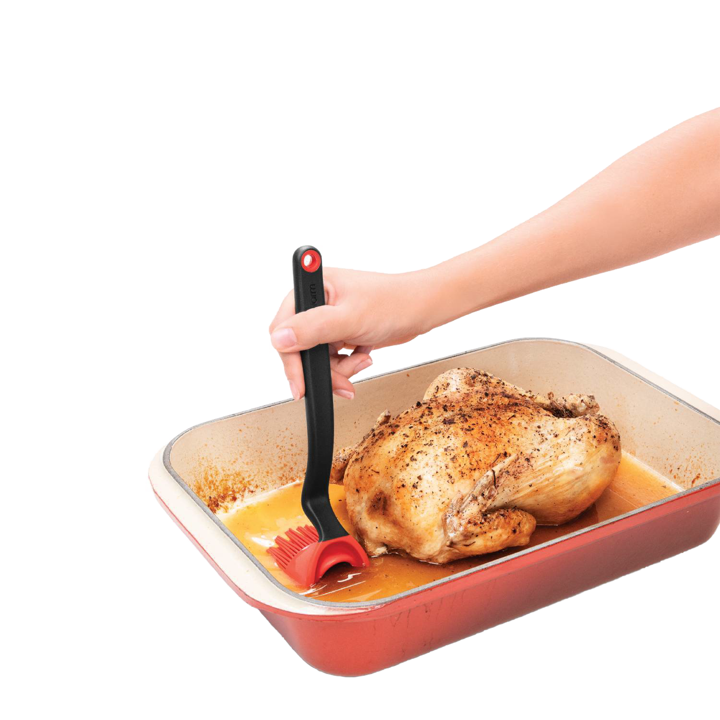 Hand using black and red silicone basting brush to baste roasted chicken in red roasting pan for kitchenware tools