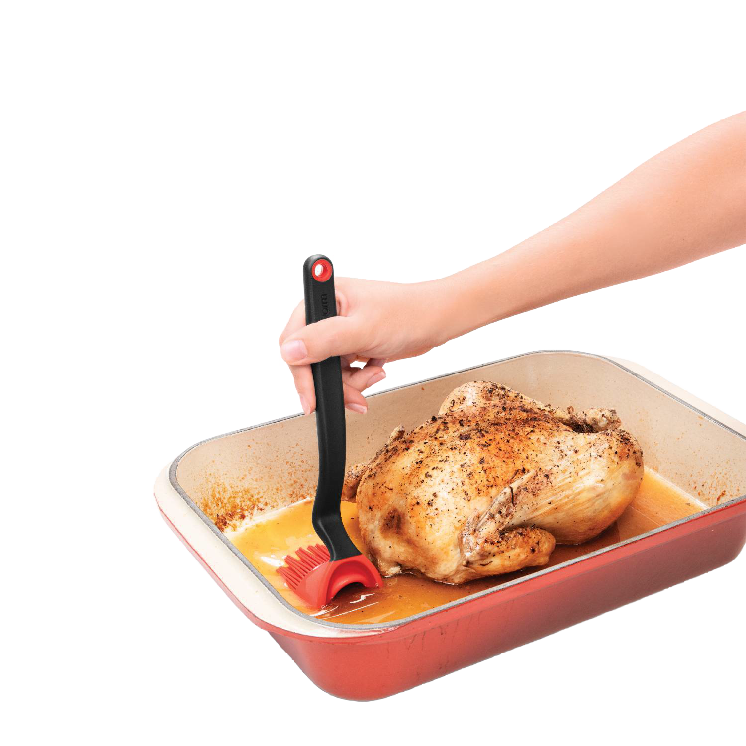 Hand using black and red silicone basting brush to baste roasted chicken in red roasting pan for kitchenware tools