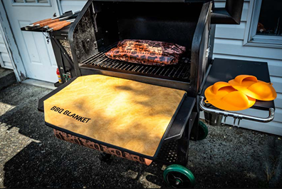 Light brown insulated BBQ blanket draped over grill shelf with black trim for heat retention during cooking tasks