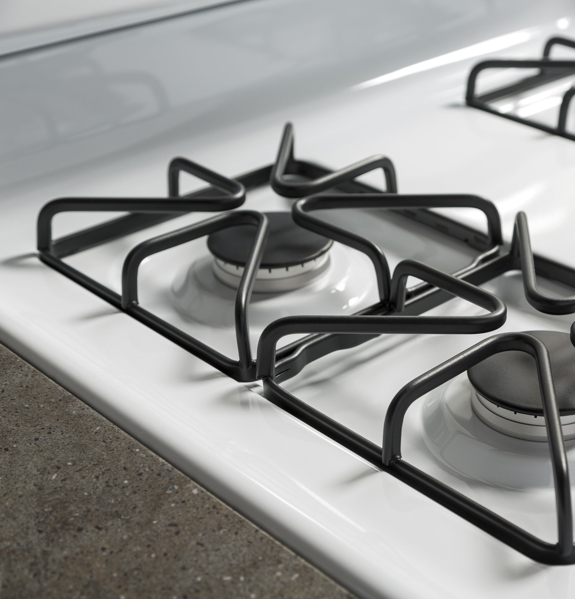 Close-up of black cast iron grates over white surface burners on gas cooktop in kitchen appliance and home improvement collections
