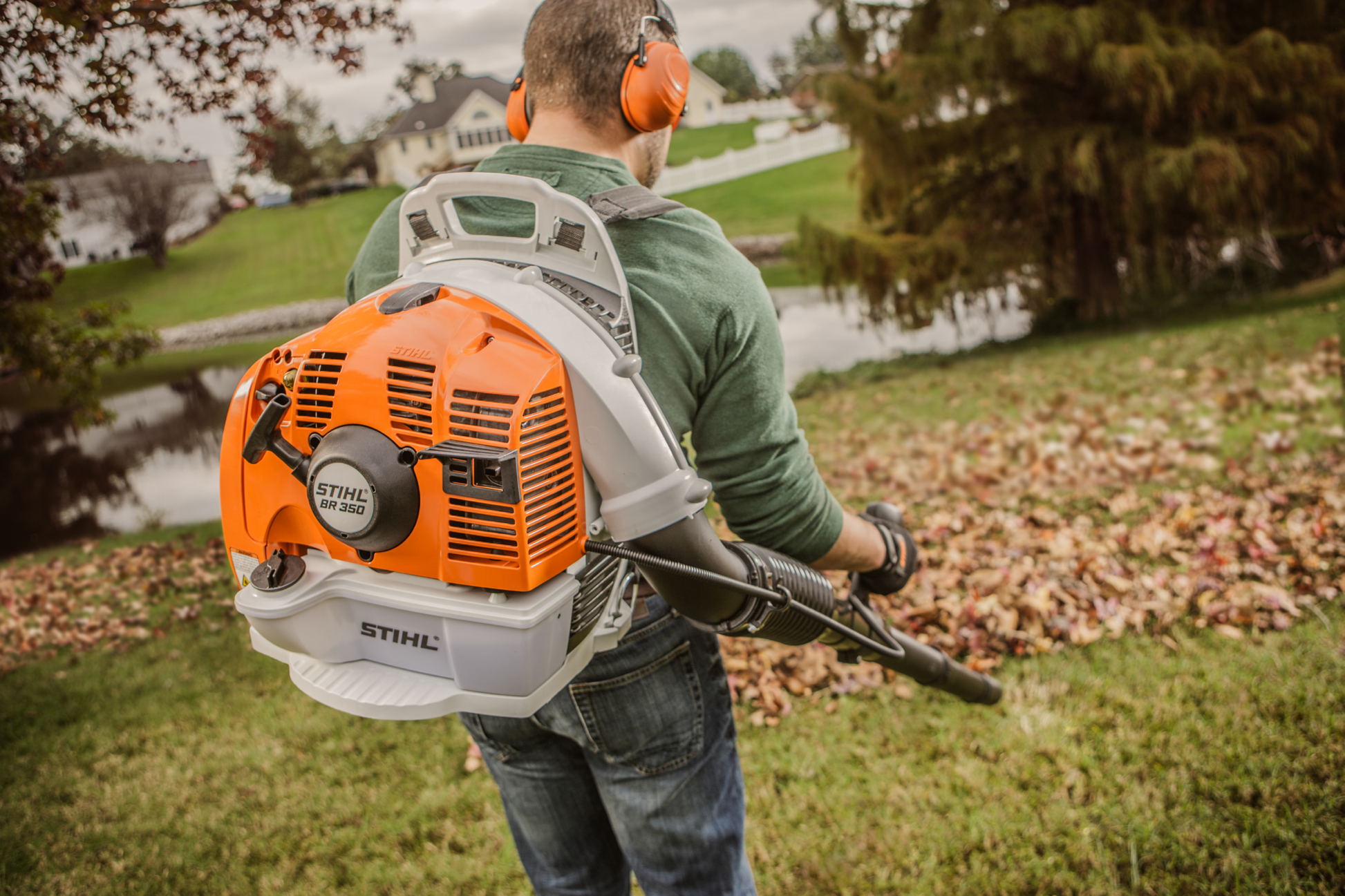 Man wearing noise protection using orange and white backpack blower with ergonomic straps for yard cleanup tasks